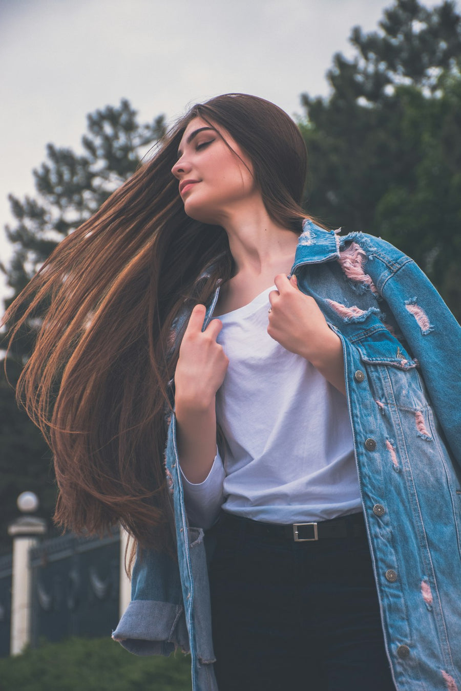 Mujer joven de cabello largo castaño, con chamarra de mezclilla, al aire libre