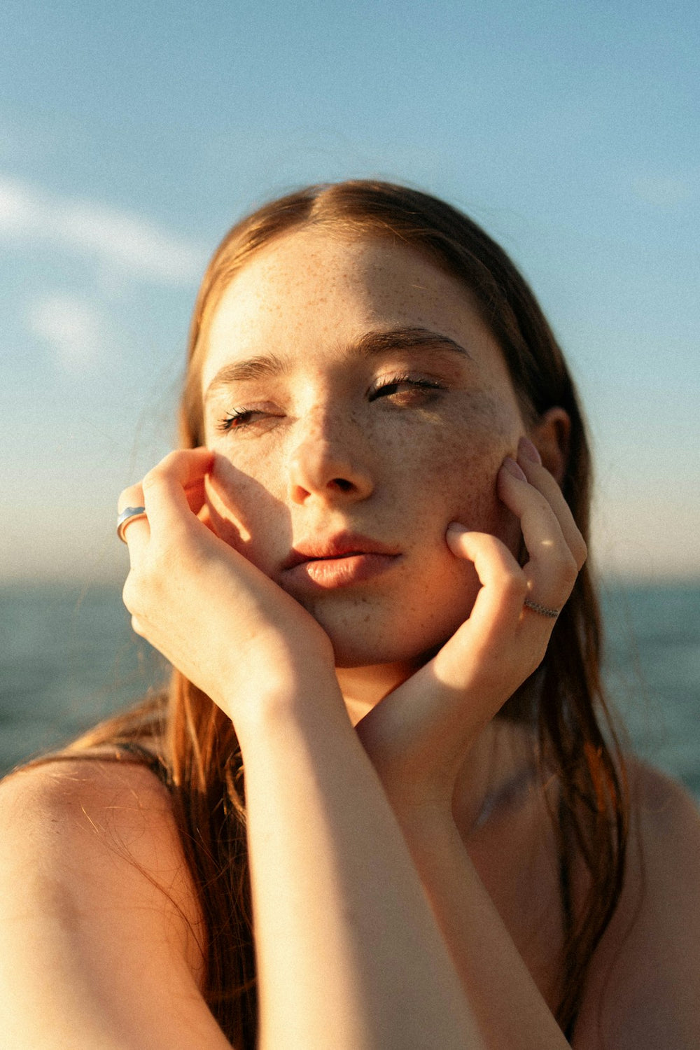 Mujer joven con pecas, con las manos en la cara y luz dorada del atardecer