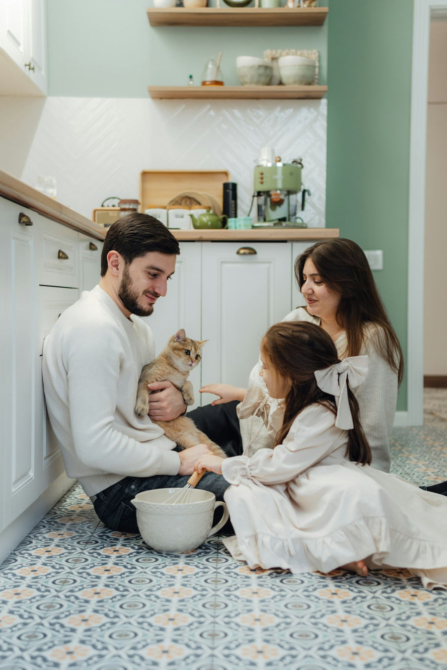 Papá, mamá y su hija sentados en el piso de la cocina, jugando con un gato