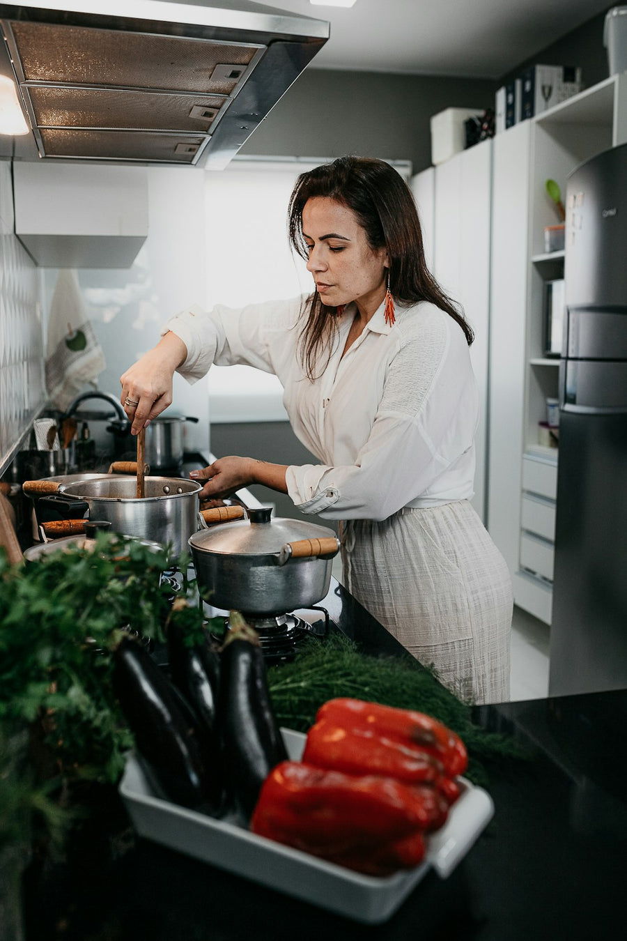 Mujer cocinando en su cocina con berenjenas, pimientos y hojas verdes sobre la barra