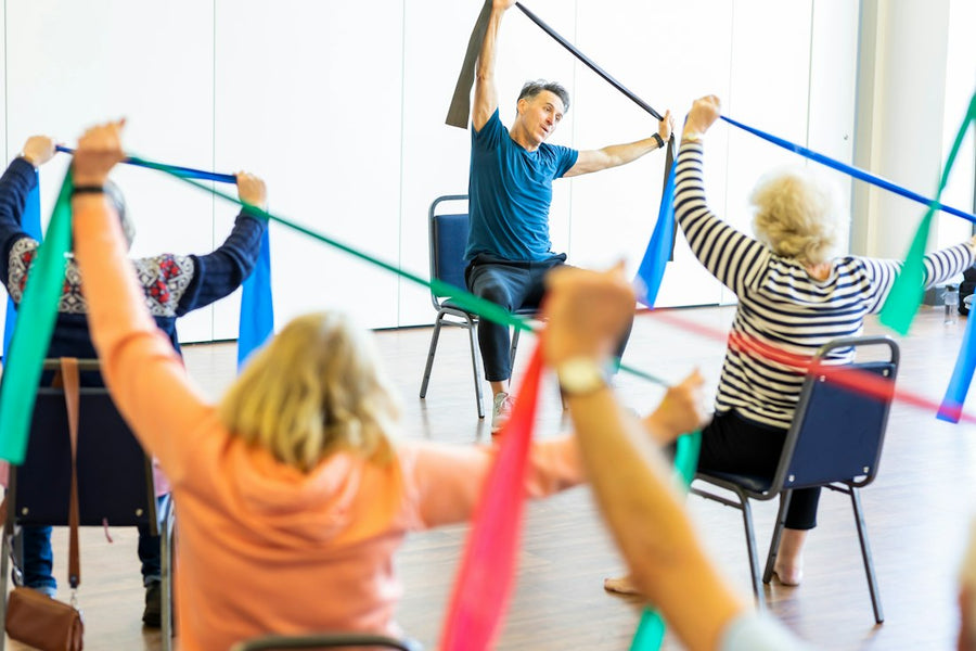 Grupo de adultos mayores haciendo ejercicio sentados con ligas de colores