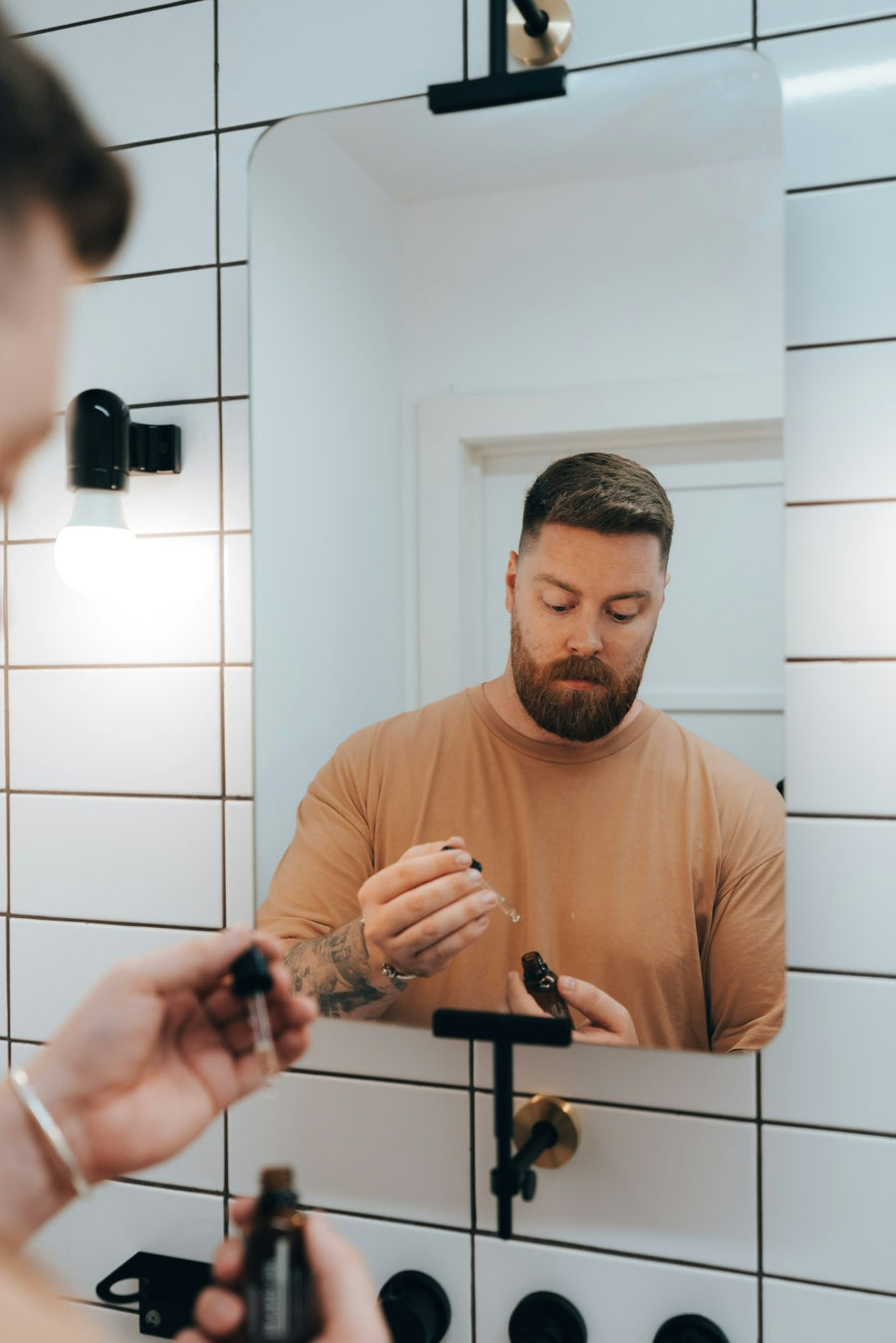 Hombre con barba aplicándose sérum en la cara frente al espejo del baño