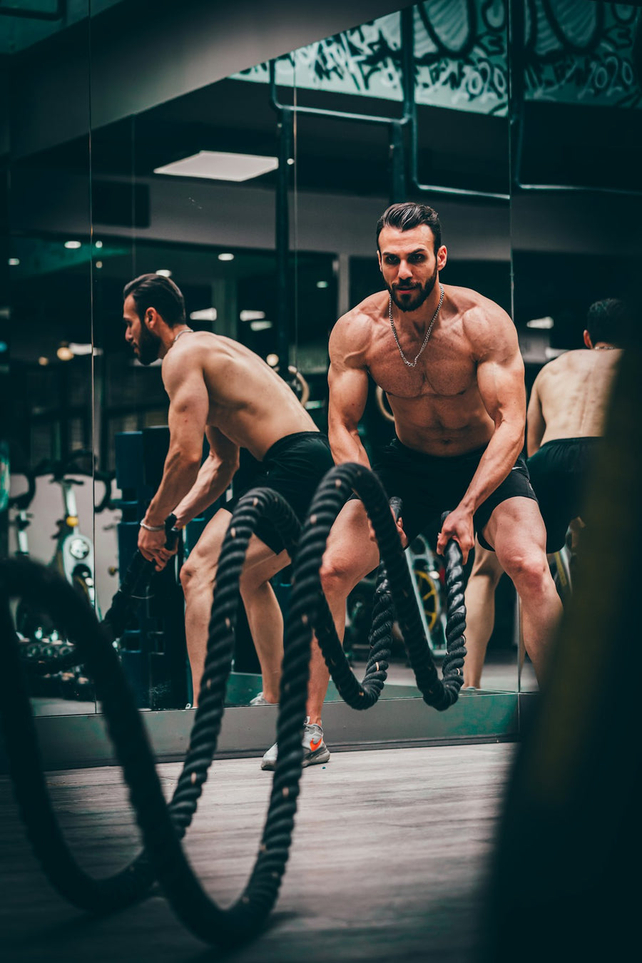 Hombre joven y musculoso entrenando con cuerdas de batalla en el gimnasio