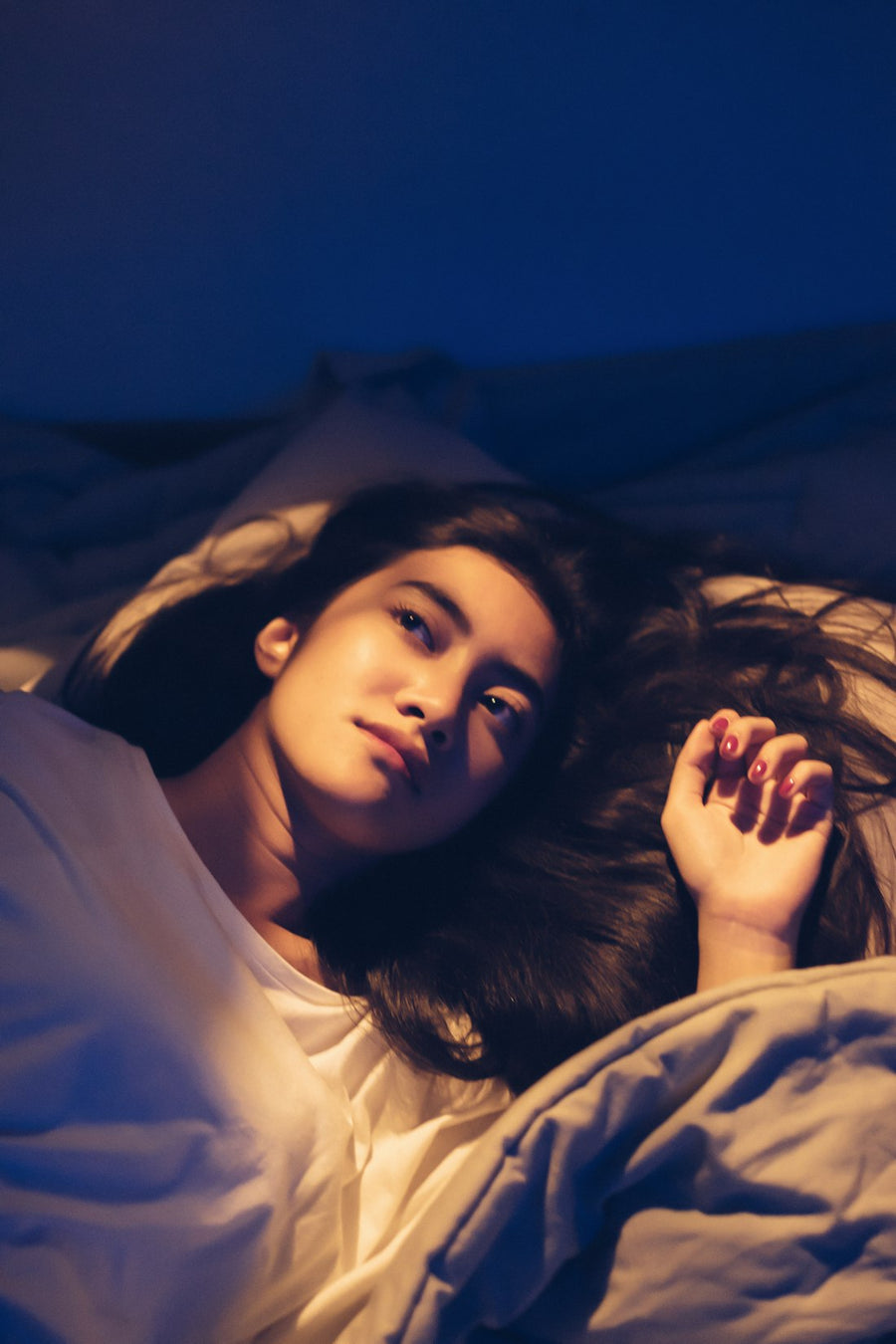 Mujer despierta en la cama de noche, mirando al techo con luz tenue
