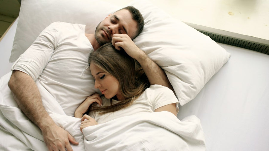 Pareja durmiendo abrazada en una cama blanca